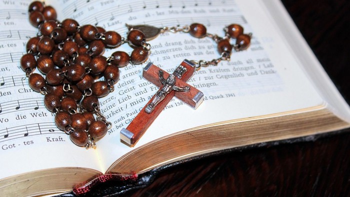 Rosenkranzperlen und Kreuz auf einem aufgeschlagenen Buch