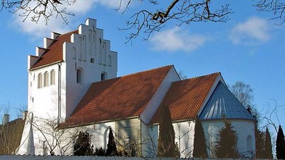 Et hvidt kirkebygning med røde tag og en klokketårn i en snedækked landskab