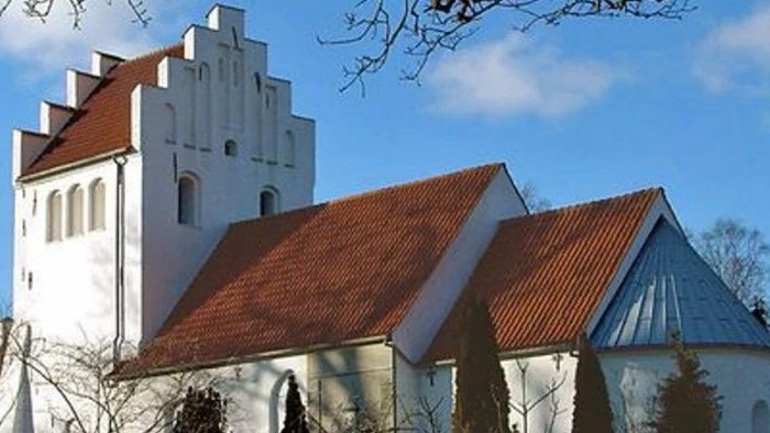 Et hvidt kirkebygningskompleks med røde tag og en tårn.