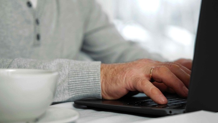 Person, der skriver på en bærbar computer, mens de holder en kop kaffe ved siden af sig.