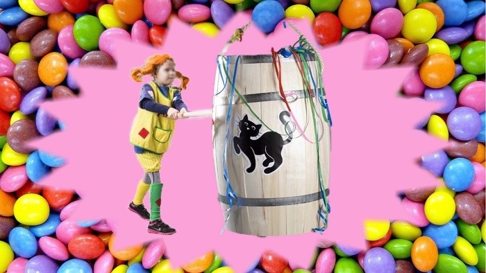 En pige i en gul dragt trækker en drage formet som en tønde med et sort katte-design mellem farverige slik.