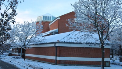 Et murstensbygning dækket af sne med træer og en klar vinterhimmel i baggrunden.