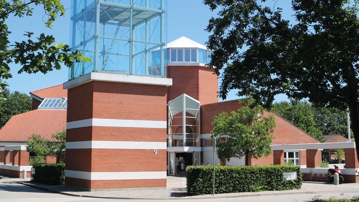 Et moderne glasbygning i en parkagtig omgivelse