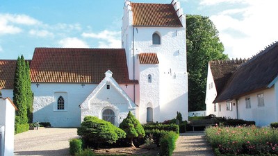 En smuk og hvid kirke med tårn og røde tag i en trædit og grønne omgivelser