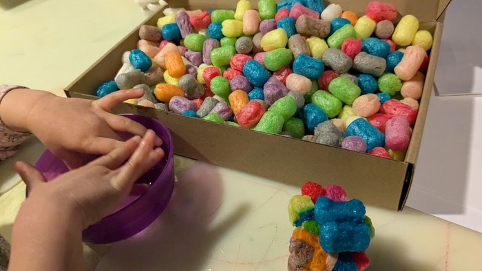 Kinderhände greifen in eine Schachtel mit bunten Süßigkeiten.