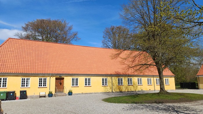 Gul bygning med rødt tag og træer foran