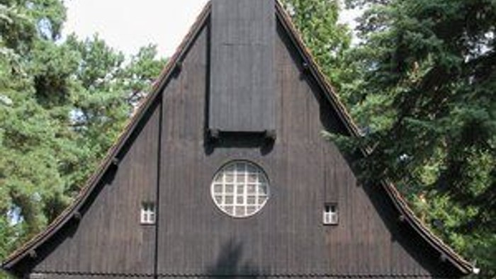 Das Bild zeigt eine hölzerne Kirche mit einem Turm und einem grünen Eingang.