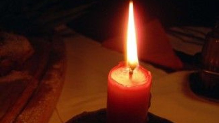 Eine rote Kerze brennt auf einem Holztisch.