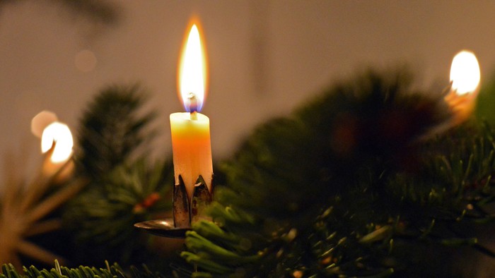 Eine brennende Kerze auf einem Weihnachtsbaum mit Lichtern im Hintergrund
