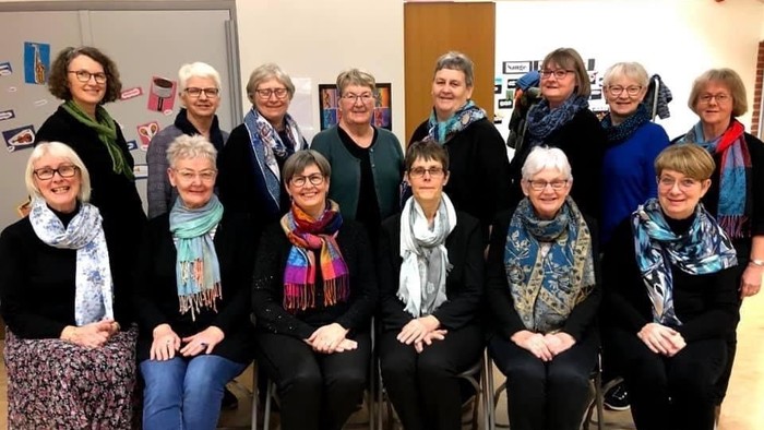 En gruppe kvinder samlet til et møde eller fest, alle med skarver og muntert udseende.