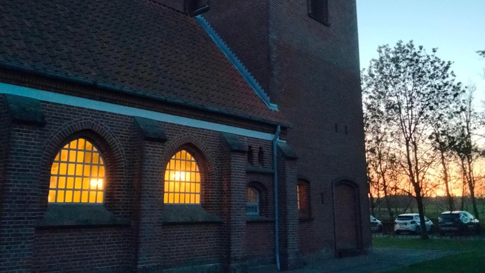 En murstenet kirke med spids tak og lysende vinduer ved solnedgang