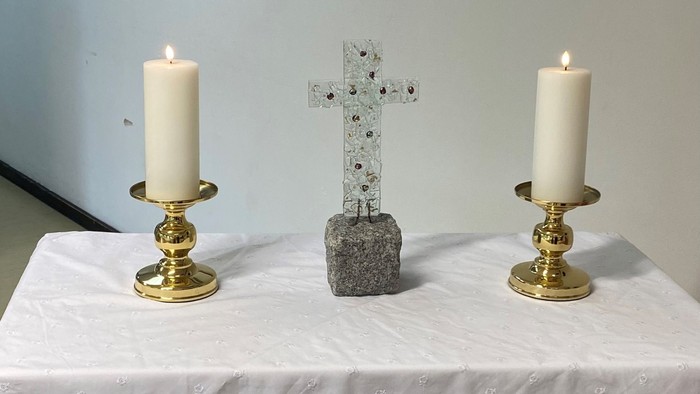 To alteret er dekket med et hvidt tøj med blomster, og der er to lysstake med lysede lygter på hver side af et sten kors.