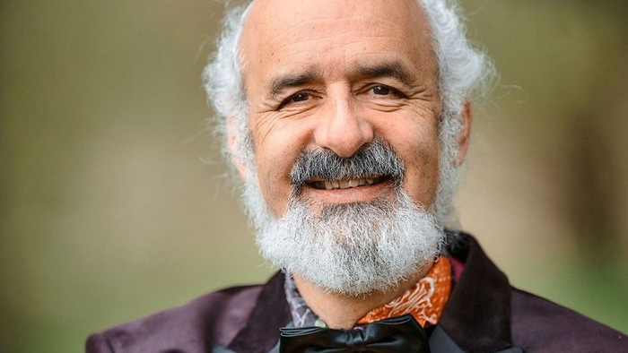 En smilende mand med hvidt skæg og overskæg i jakkesæt, slips og butterfly udendørs.