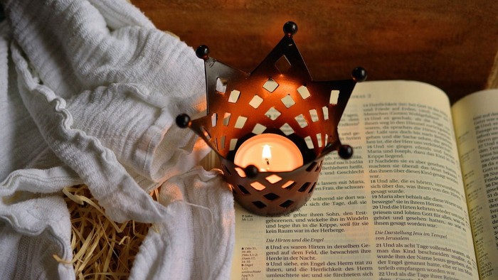 Eine Kerze im Halter steht auf einem Buch und einer Decke.