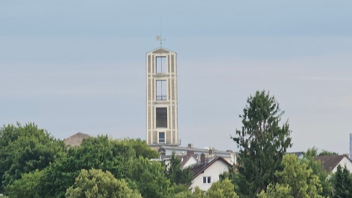 Hoher Uhrturm, umgeben von Bäumen und Häusern.
