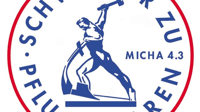 Das Bild zeigt ein kreisförmiges Logo mit einer blauen Figur, die einen Hammer hebt, umgeben von deutschem Text und der Aufschrift *„Micha 4.3“* am unteren Rand.