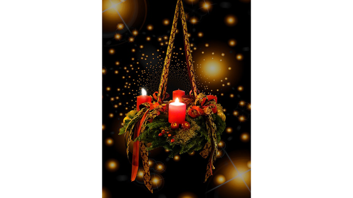 Ein hängender Adventskranz mit drei brennenden Kerzen und Weihnachtsdekorationen vor einem dunklen Hintergrund mit Lichtern.