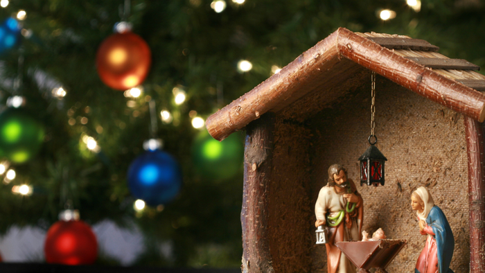 Small nativity scene in front of Christmas tree with ornaments.