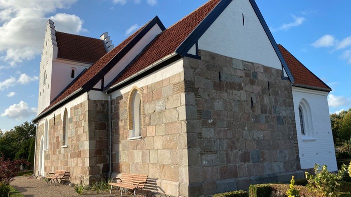 En lille kirke med tårn og benker udenfor