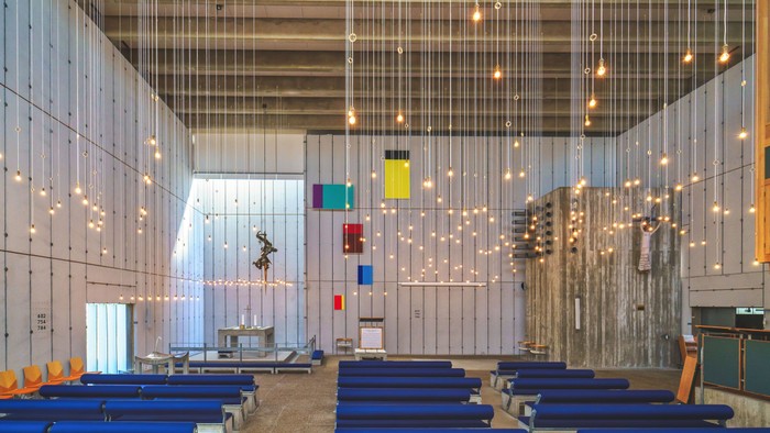 Indre del af moderne kirke med blå bænke og lysstykker.