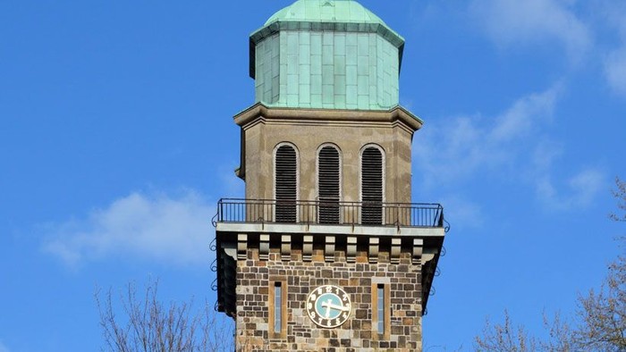 Die Erlöserkirche im Ortsteil Hiltrop mit Gipfelkreuz und Turmuhr vor einem strahlend blauen Himmel.