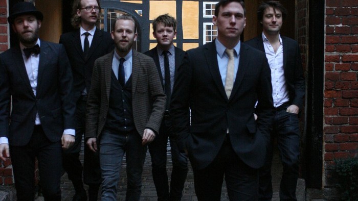 En gruppe mænd i formelle klæder går gennem en bue.