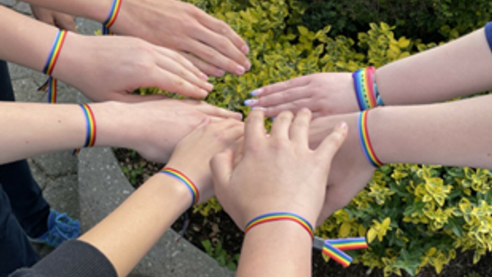 Mehrere Hände mit Regenbogenarmbändern sind ineinander verschränkt.