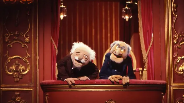 To muppetfigurerne sidder på en prægtig scene med røde gardiner og gyldne detaljer.
