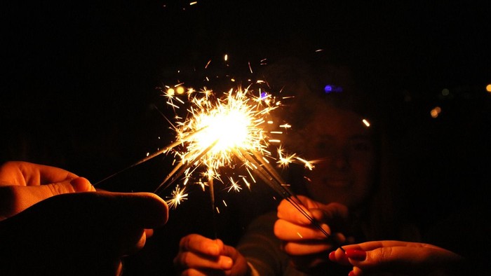 Zwei Hände halten ein brennendes Feuerwerk in der Dunkelheit