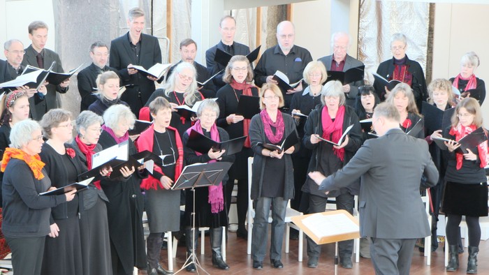 Ein Chor probt unter Leitung eines Dirigenten in einem Saal