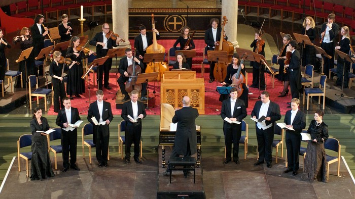 Ein Orchester probt in einem großen Saal unter der Leitung eines Dirigenten
