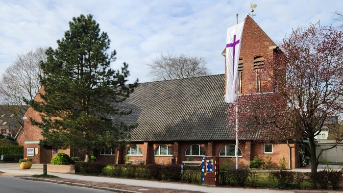 Kirchengebäude mit Fahnen und Bäumen vor blauem Himmel