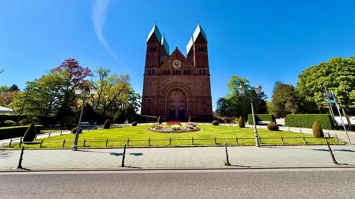 Beeindruckende Backsteinkathedrale mit Zwillingstürmen, gelegen in einem gepflegten, landschaftlich gestalteten Innenhof unter klarem Himmel.