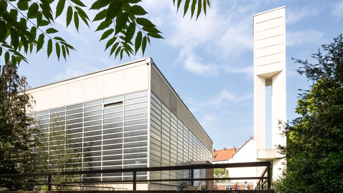 Moderne Kirche mit hohem Turm und Glasfassade, umgeben von Bäumen