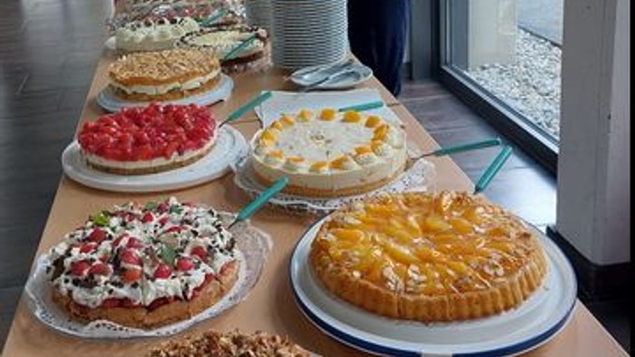 Mehrere Kuchen, die auf einem Tisch ausgestellt sind, mit Menschen, die in der Nähe stehen.