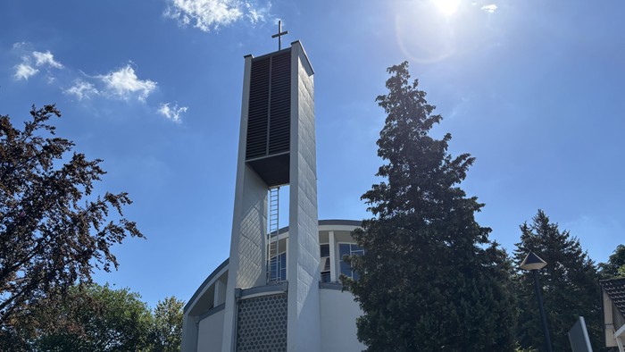 Moderne Kirche mit hohem Glockenturm vor strahlend blauem Himmel und umgeben von Grün.
