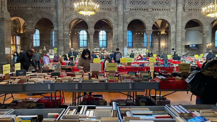 Marché de livres dans une grande salle avec des arches et des fenêtres en vitraux.