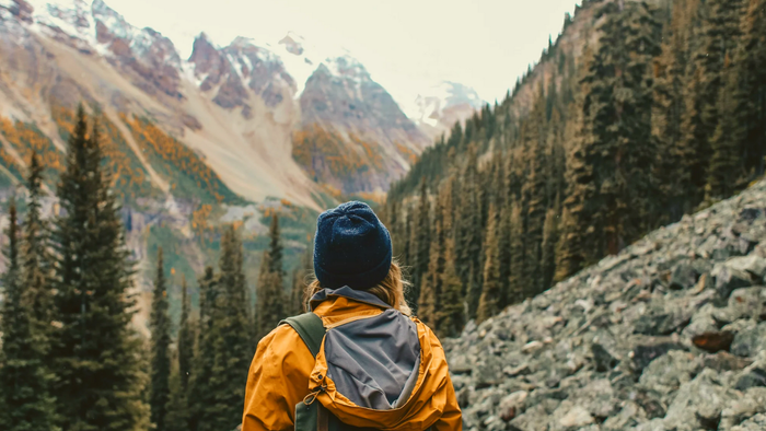 Person steht auf felsigem Pfad vor Bergen mit Rucksack
