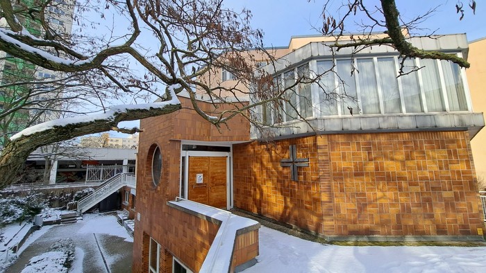 Das Bild zeigt ein modernes Holzgebäude neben einem Baum im Schnee.