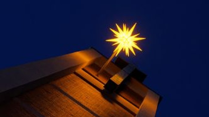 Ein beleuchtetes Holzhaus bei Nacht mit einem hellen Stern am Himmel.