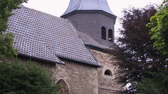 Historische Steinkirche mit einem markanten Kuppelturm, umgeben von üppigem Grün.