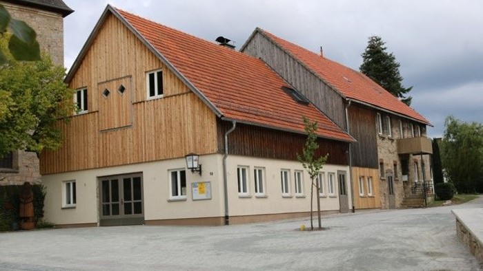 Traditionelles Holzscheunen-Gebäude mit rotem Ziegeldach und modernem Eingang in einem ruhigen Innenhof.