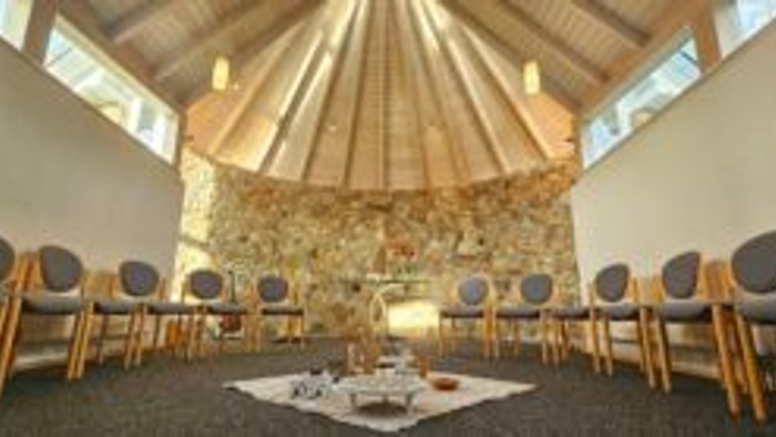 Ein ruhiger Raum mit Stühlen und einem Tisch in der Mitte, umgeben von Fenstern und einer Steinsäule.