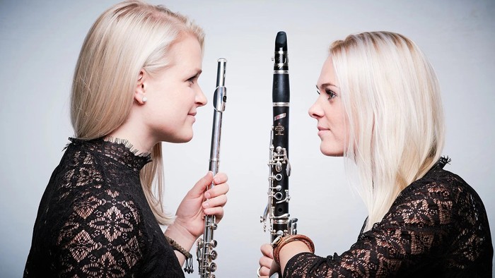 To kvinder, der holder klarinetter, iført sorte kniplinger, vendt mod hinanden.