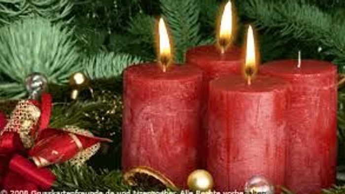 Drei brennende rote Adventskerzen vor grünem Tannenbaum.