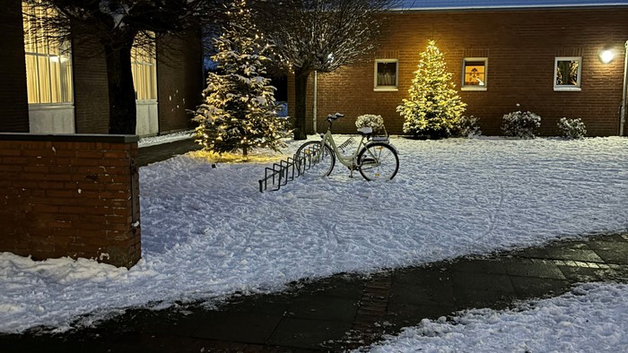 Schneebedeckte Straße mit zwei Fahrrädern und Weihnachtsbäumen vor Haus