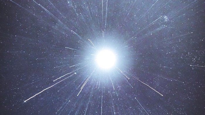 Ein helles Licht strahlt in die Dunkelheit, umgeben von zahlreichen weißen Linien und kleinen Punkten.