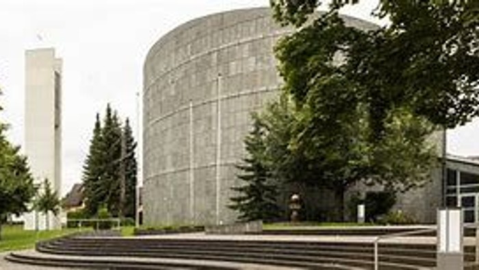 Moderner Bau mit geschwungener Architektur, umgeben von Bäumen und einem Gehweg.