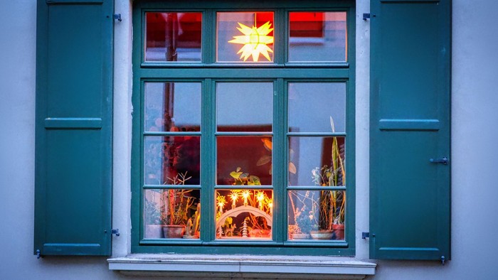 Ein Fenster mit grünen Fensterläden und einer beleuchteten Weihnachtsdekoration im Inneren