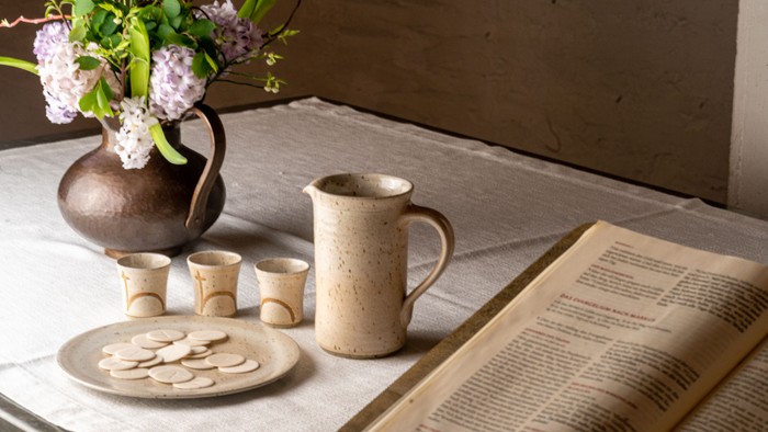 Auf dem Altar stehen Tonteller mit Oblaten und Tonkrug mit drei kleinen Einzelkelchen nebst Bibel und Blumen - alles ist bereit für das Abendmahl.